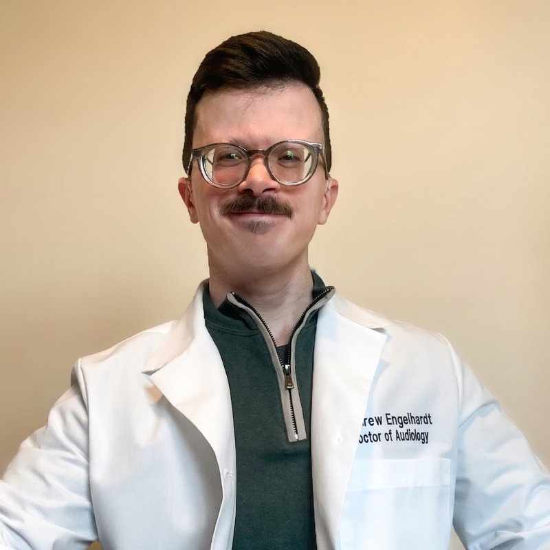 Dr. Andrew Engelhardt, audiologist, smiling in glasses and a white Doctor of Audiology coat